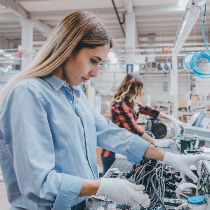 Produktion & Qualitätsmanagement - Zwei Frauen arbeiten in einer modernen Produktionshalle an elektronischen Bauteilen.