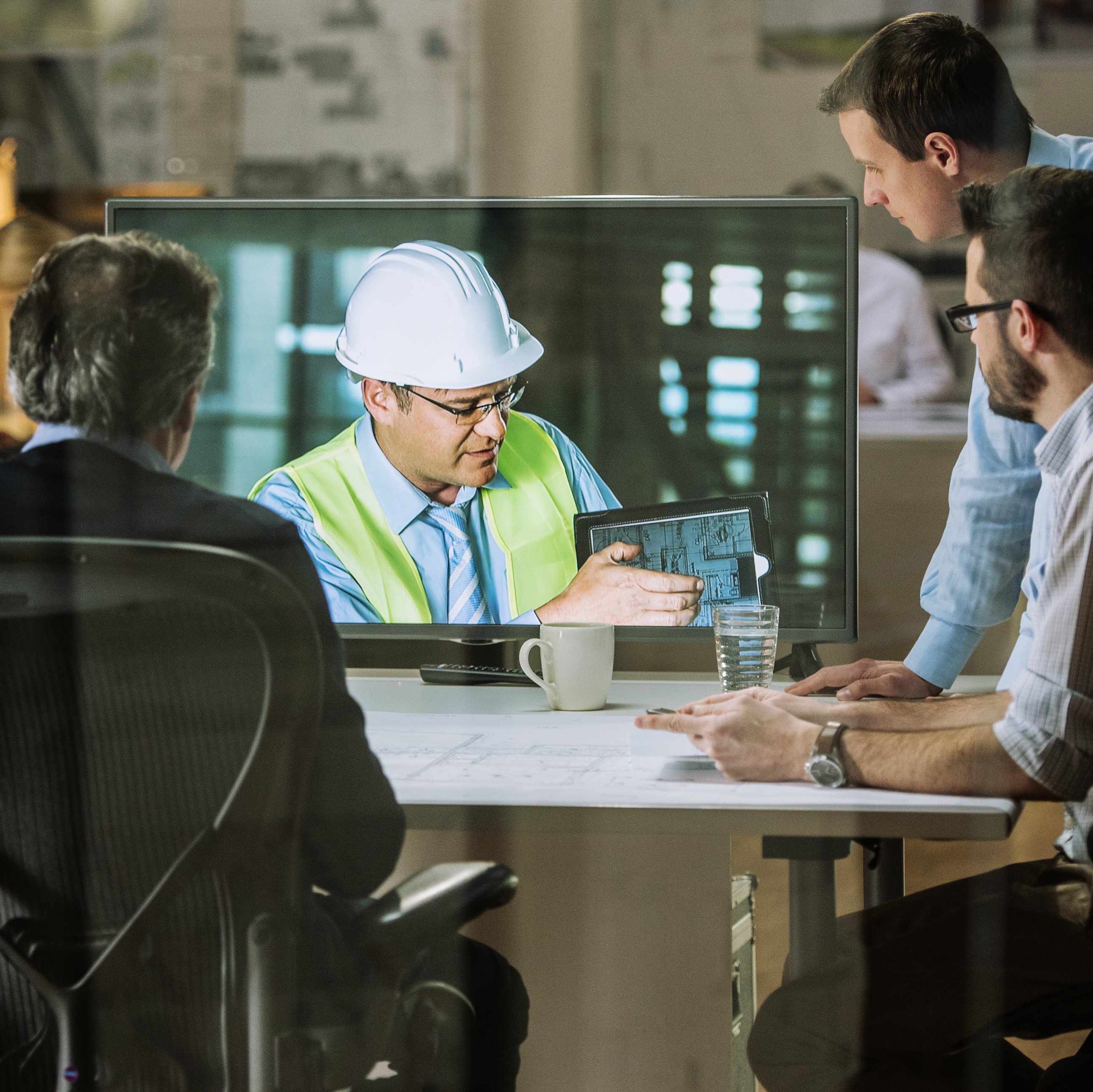 Informations- und Kommunikationstechnik: Eine Gruppe von Mitarbeitern nimmt an einer Videokonferenz mit einem Ingenieur Teil, der Pläne erläutert.