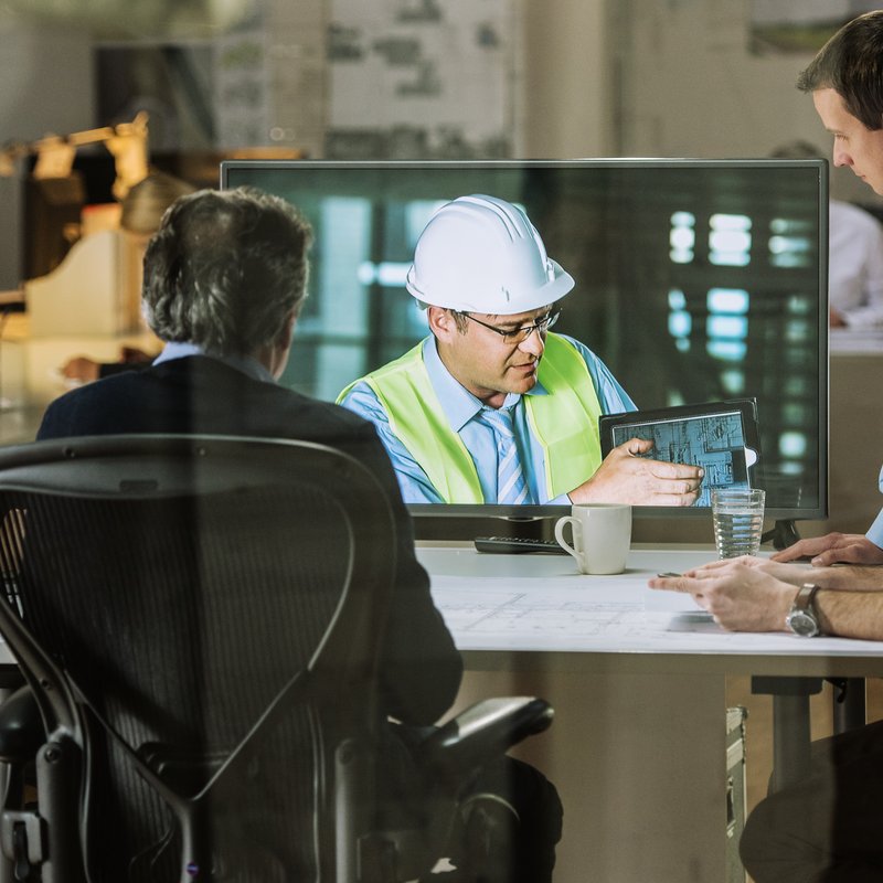 Informations- und Kommunikationstechnik: Eine Gruppe von Mitarbeitern nimmt an einer Videokonferenz mit einem Ingenieur Teil, der Pläne erläutert.
