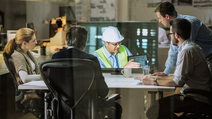 Informations- und Kommunikationstechnik: Eine Gruppe von Mitarbeitern nimmt an einer Videokonferenz mit einem Ingenieur Teil, der Pläne erläutert.