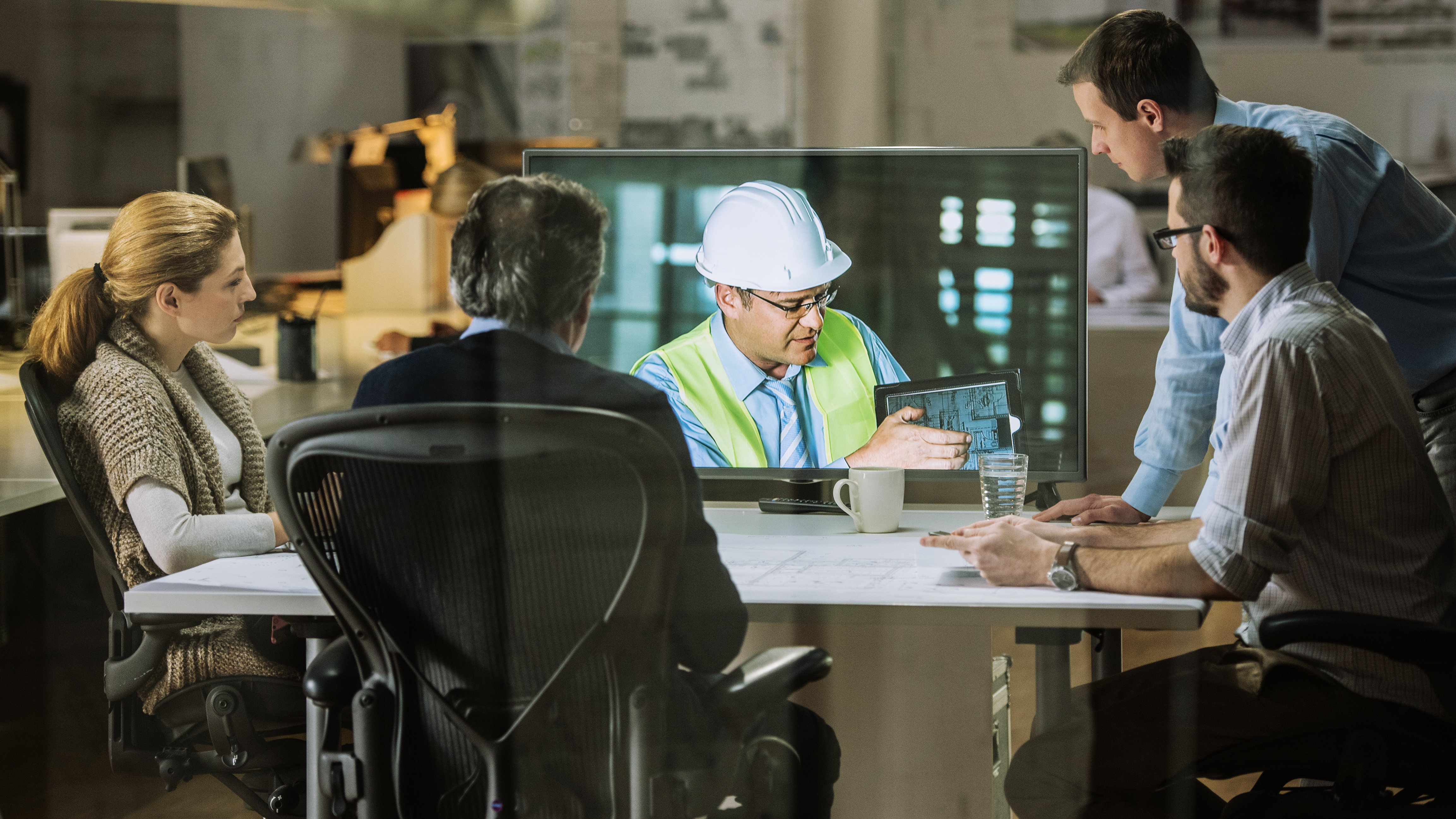 Informations- und Kommunikationstechnik: Eine Gruppe von Mitarbeitern nimmt an einer Videokonferenz mit einem Ingenieur Teil, der Pläne erläutert.