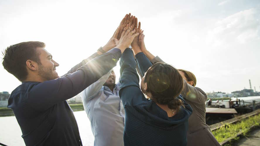 Eine Gruppe von Menschen gibt sich ein gemeinsames High-Five, symbolisierend Teamwork.